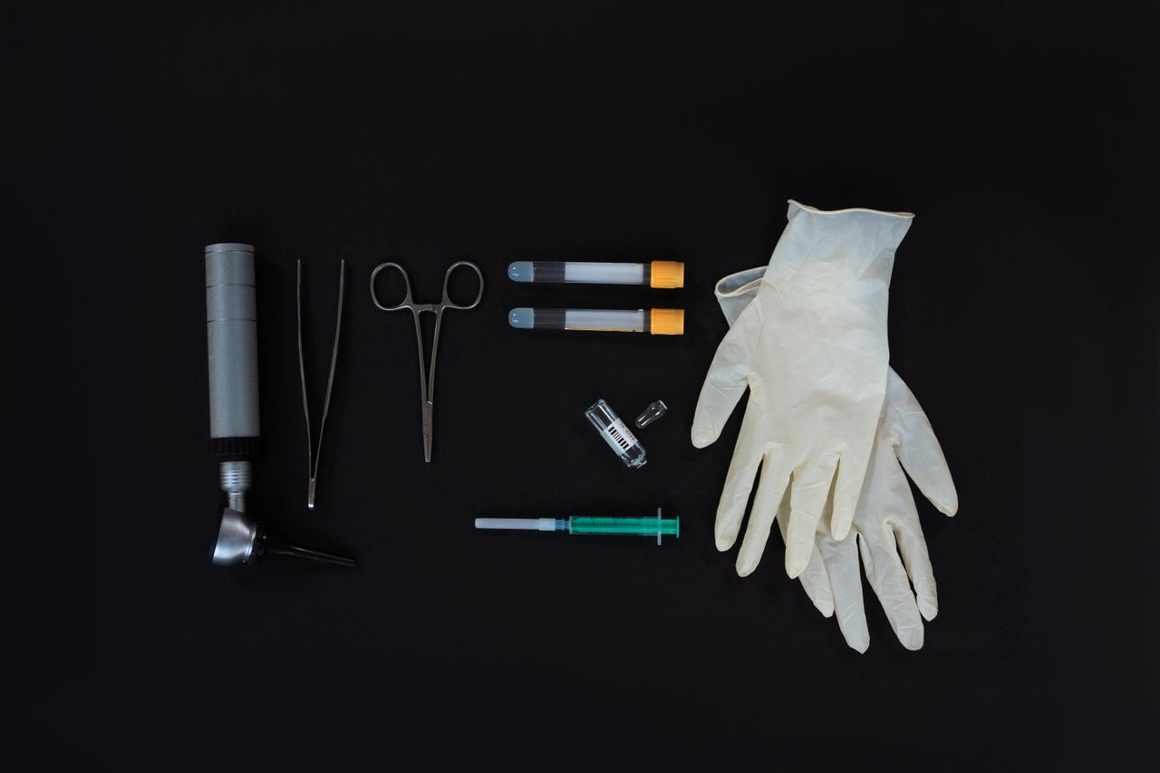 Flat lay of essential medical tools on a black background, including gloves and syringe.